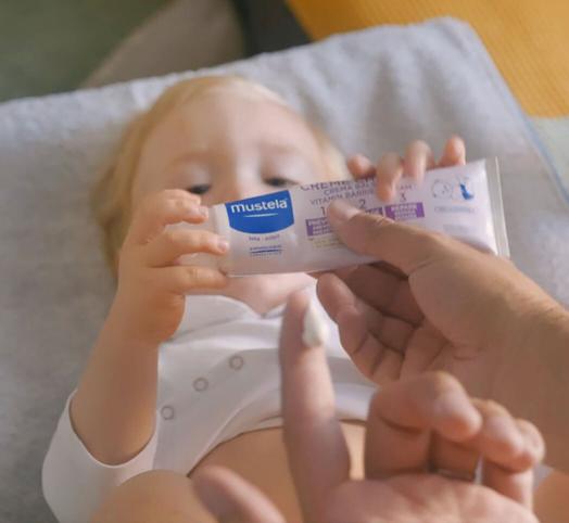 Bébé qui tient dans ses mains la crème change Mustela