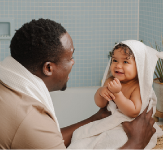 Bébé métisse avec une cape de bain qui sort du bain et qui est porté par son papa