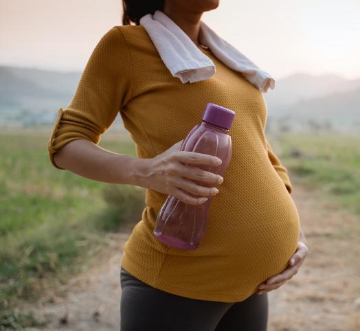 Femme enceinte qui se touche le ventre et qui porte une gourde rose dans sa main