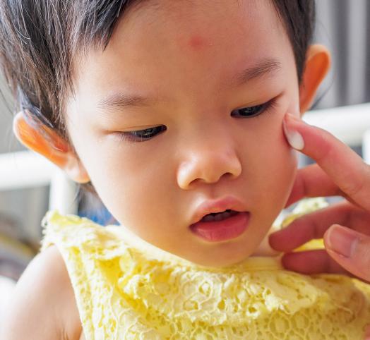 Visage d'un enfant asiatique avec une main qui lui applique de la crème sur la joue